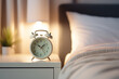 © Anna - A cozy bedroom scene featuring a classic white alarm clock sitting on a bedside table next to a soft bed with white sheets