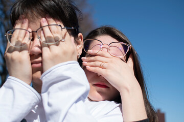 Wall Mural - Conceptual portrait of a two women in eyeglasses. Young attractive women covering her faces with a her hands	