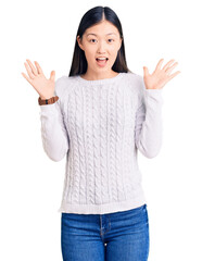 Wall Mural - Young beautiful chinese woman wearing casual sweater celebrating crazy and amazed for success with arms raised and open eyes screaming excited. winner concept