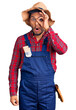 Handsome latin american young man weaing handyman uniform doing ok gesture shocked with surprised face, eye looking through fingers. unbelieving expression.