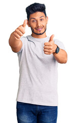 Wall Mural - Handsome latin american young man wearing casual tshirt approving doing positive gesture with hand, thumbs up smiling and happy for success. winner gesture.