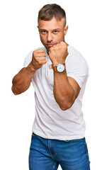 Canvas Print - Handsome muscle man wearing casual white tshirt ready to fight with fist defense gesture, angry and upset face, afraid of problem