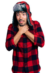 Canvas Print - Hispanic young man with beard wearing fluffy earmuff hat shouting and suffocate because painful strangle. health problem. asphyxiate and suicide concept.