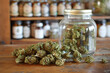 Cannabis (or hemp or marijuana) dried flower buds in a glass jar on a wooden shop counter, choice of bottles of CBD oil in the background, medicinal legal cannabis,  natural alternative medicine