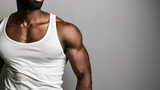 Fototapeta Na drzwi - A black man with a beard wearing a white tank top, standing against a plain grey background. Partial view of torso, unrecognizable man