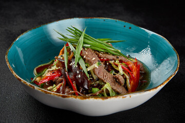 Canvas Print - Asian salad with beef and vegetables in ceramic bowl on dark concrete background. Salad with beef fillet, muer mushrooms and green onion in chinese cuisine style. Asian menu in minimal style on black.