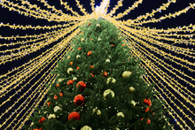 New Year Christmas Tree Decorated Christmas Balls With Yellow Flickering Lights Of Garlands And White Star Topper On Green Tree At Night, Merry Christmas And Happy New Year Mood With Twinkling Lights