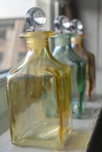 Vertical Shot Of Yellow And Green Glass Jars On A Window Sill.