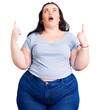 Young plus size woman wearing casual clothes amazed and surprised looking up and pointing with fingers and raised arms.