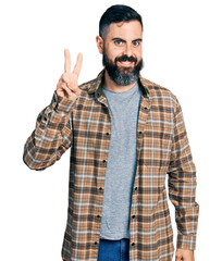 Wall Mural - Hispanic man with beard wearing casual shirt showing and pointing up with fingers number two while smiling confident and happy.