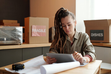 Poster - Young serious female solopreneur with tablet looking through online issues on screen while sitting by workplace in cafe under refit