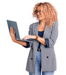 Young blonde woman with curly hair working using laptop looking positive and happy standing and smiling with a confident smile showing teeth