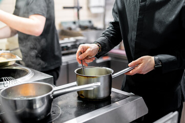 Wall Mural - A chef stirs a pot on a stove, showcasing the active preparation of a meal in a professional kitchen setting. The image captures the hands-on aspect of culinary arts