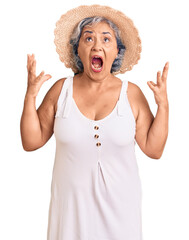 Sticker - Senior woman with gray hair wearing summer hat and summer clothes crazy and mad shouting and yelling with aggressive expression and arms raised. frustration concept.