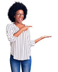 Poster - Young african american woman wearing casual clothes and glasses amazed and smiling to the camera while presenting with hand and pointing with finger.