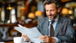 © amixstudio - Professional man reviewing documents in a cafe with a cup of coffee.