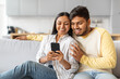 © Prostock-studio - Indian Man and Woman Sitting on Couch Looking at Cell Phone