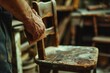 A close-up shot captures the skilled hands of a craftsman as they meticulously sand down the armrest of a vintage wooden chair. 
