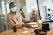 African businessman in a mask sitting at his office desk