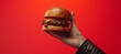 a person's hand holding up a meaty burger against a red background
