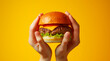 hands holding a hamburger above yellow background