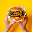 The first person viewed photo of a woman's two hand holding a burger on wrapping paper.