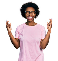 Wall Mural - African american woman with afro hair wearing casual clothes and glasses gesturing finger crossed smiling with hope and eyes closed. luck and superstitious concept.