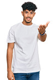 Fototapeta Koty - Young arab man wearing casual white t shirt smiling friendly offering handshake as greeting and welcoming. successful business.