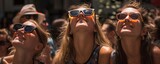 Fototapeta Przestrzenne - Women wearing black and orange solar eclipse glasses look up at the sky surrounded by other people