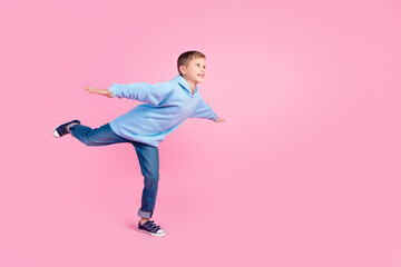 Wall Mural - Full size profile portrait of cheerful schoolchild stand one leg hands wings look empty space isolated on pink color background