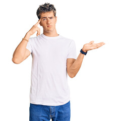 Wall Mural - Young handsome man wearing casual white tshirt confused and annoyed with open palm showing copy space and pointing finger to forehead. think about it.