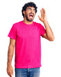 © Krakenimages.com - Handsome young man with curly hair and bear wearing casual pink tshirt shouting and screaming loud to side with hand on mouth. communication concept.