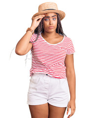 Wall Mural - Young african american woman with braids wearing summer hat worried and stressed about a problem with hand on forehead, nervous and anxious for crisis