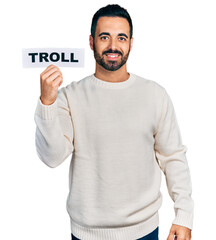 Sticker - Young hispanic man with beard holding troll banner looking positive and happy standing and smiling with a confident smile showing teeth