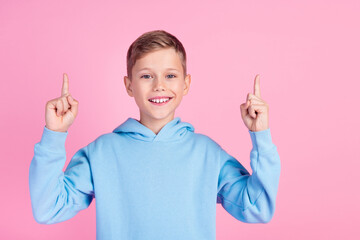 Wall Mural - Portrait of small charming boy toothy smile indicate fingers up empty space isolated on pink color background