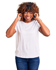 Wall Mural - Young african american woman wearing casual white tshirt covering ears with fingers with annoyed expression for the noise of loud music. deaf concept.