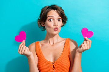 Poster - Portrait of coquettish girl with bob hairstyle wear orange knit top hold hearts postcards plump lips isolated on blue color background