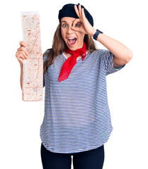 Canvas Print - Young beautiful blonde woman wearing french beret holding city map smiling happy doing ok sign with hand on eye looking through fingers