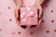  romantic pink background with male hands holding a wrapped gift box seen from above for a birthday 