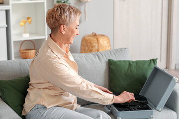 Wall Mural - Mature woman with record player sitting on sofa at home