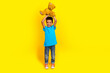 © deagreez - Full size photo of mixed race schoolboy with afro hair wear blue stylish t-shirt raising up teddy bear isolated on vivid yellow background