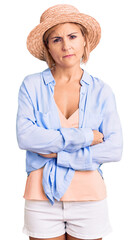 Poster - Young blonde woman wearing summer hat skeptic and nervous, disapproving expression on face with crossed arms. negative person.