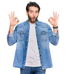 Sticker - Young hispanic man wearing casual clothes looking surprised and shocked doing ok approval symbol with fingers. crazy expression