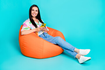 Poster - Photo of charming nice cheerful woman wear stylish print clothes comfy chair use modern iphone isolated on cyan color background