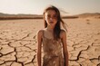 A solemn young girl in a dusty dress stands amid a vast, cracked desert, conveying a mood of isolation and climate change. Young Girl Standing in Dry Desert Landscape