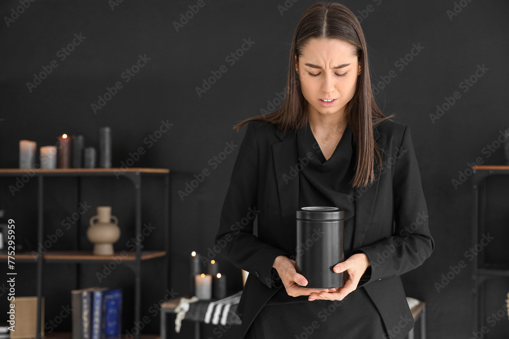 Grieving young woman with mortuary urn at funeral
