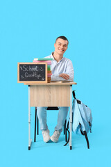 Wall Mural - Male student sitting at desk with chalkboard with text SCHOOL GOODBYE on blue background. End of school concept