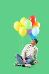 Sticker - Young man with bunch of colorful balloons sitting on green background