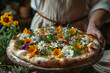 An appetizing pizza topped with a vibrant array of edible flowers, presented by a chef in a rustic kitchen setting