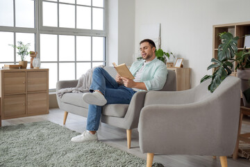 Poster - Young man reading book on grey sofa at home